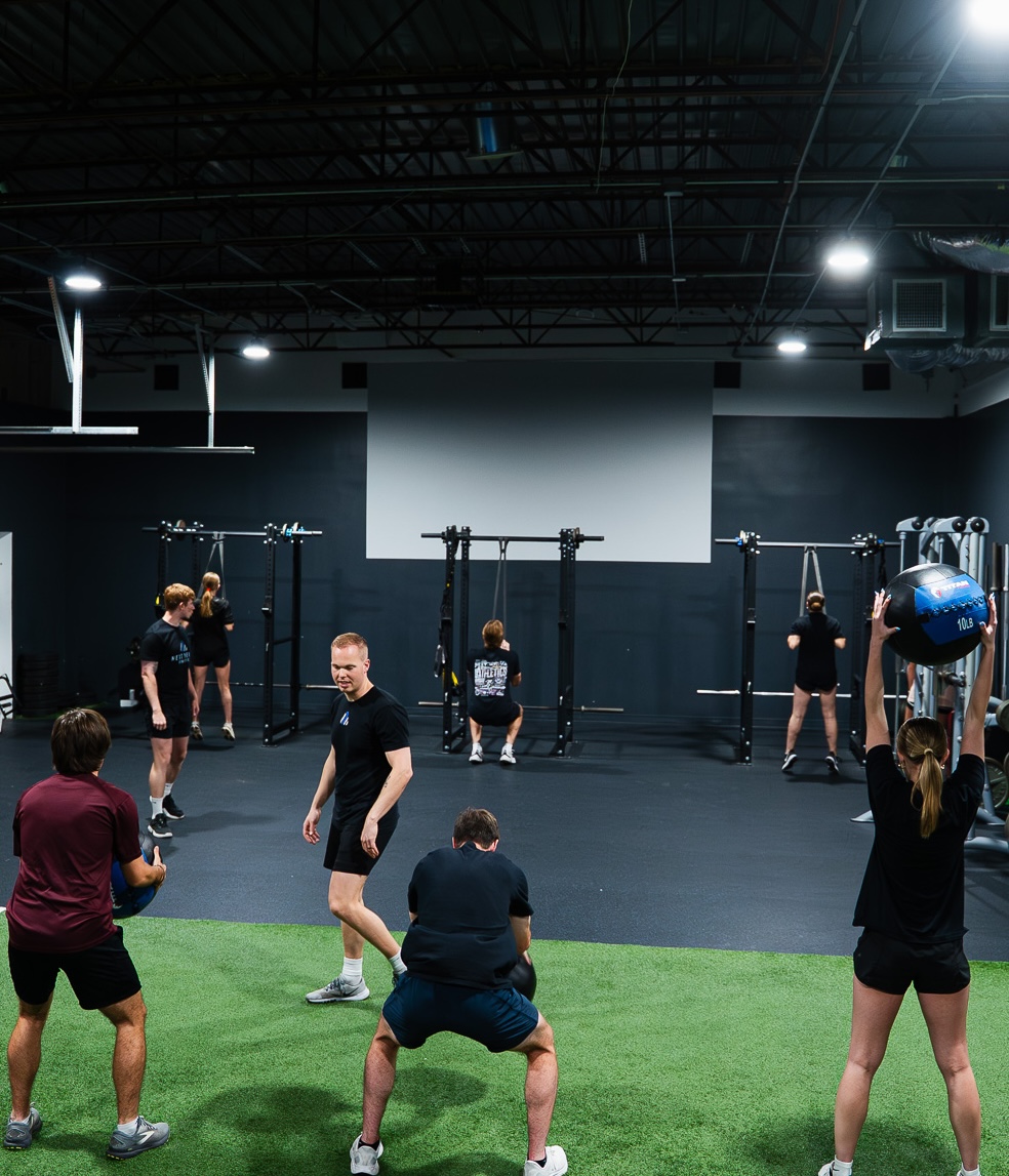NLA Performance Class in session — multiple athletes mid-workout with achievement records visible on the gym wall